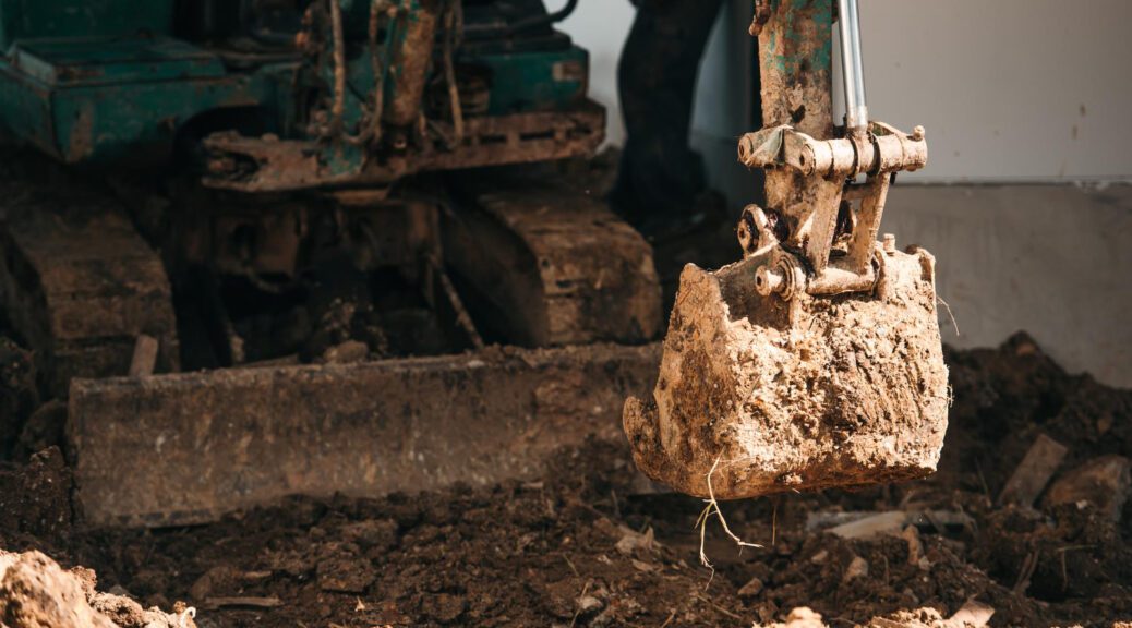 Mini ekskavatorius vykdo žemės darbus statybų aikštelėje.